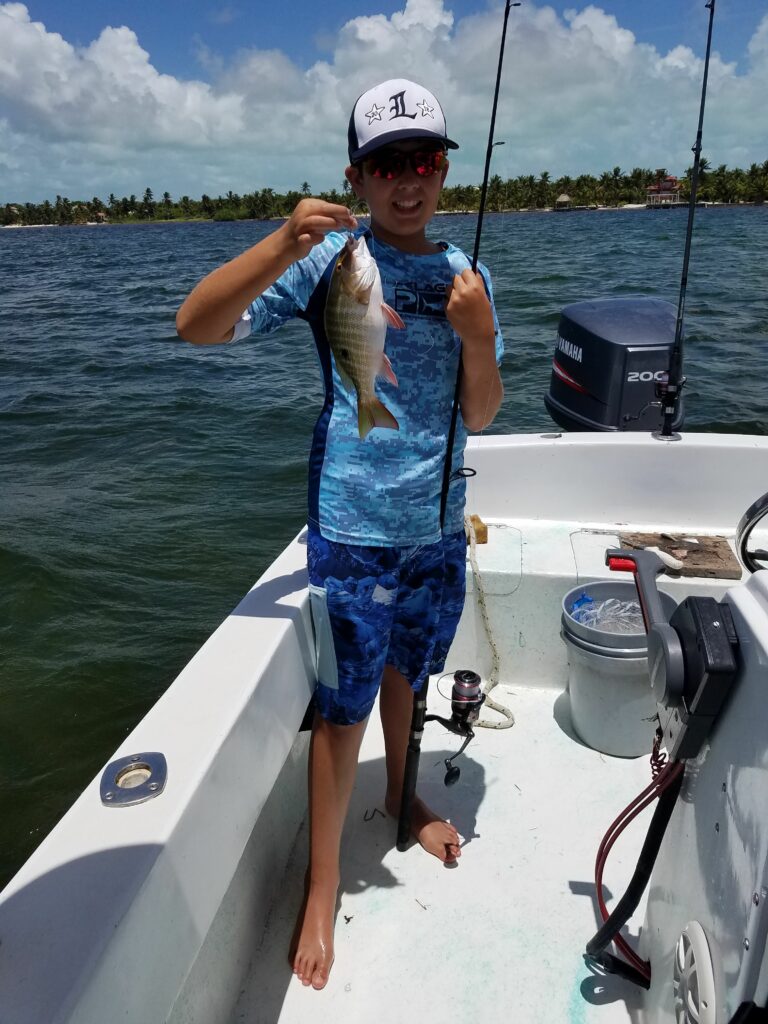 "A young angler proudly displaying his fresh catch while standing on the deck of a private fishing charter in Belize."