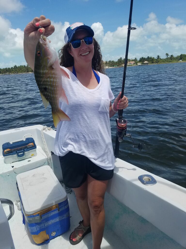 "A smiling woman on the Fish 101 boat holding up a fresh snapper she caught during a sunny day on the water."
