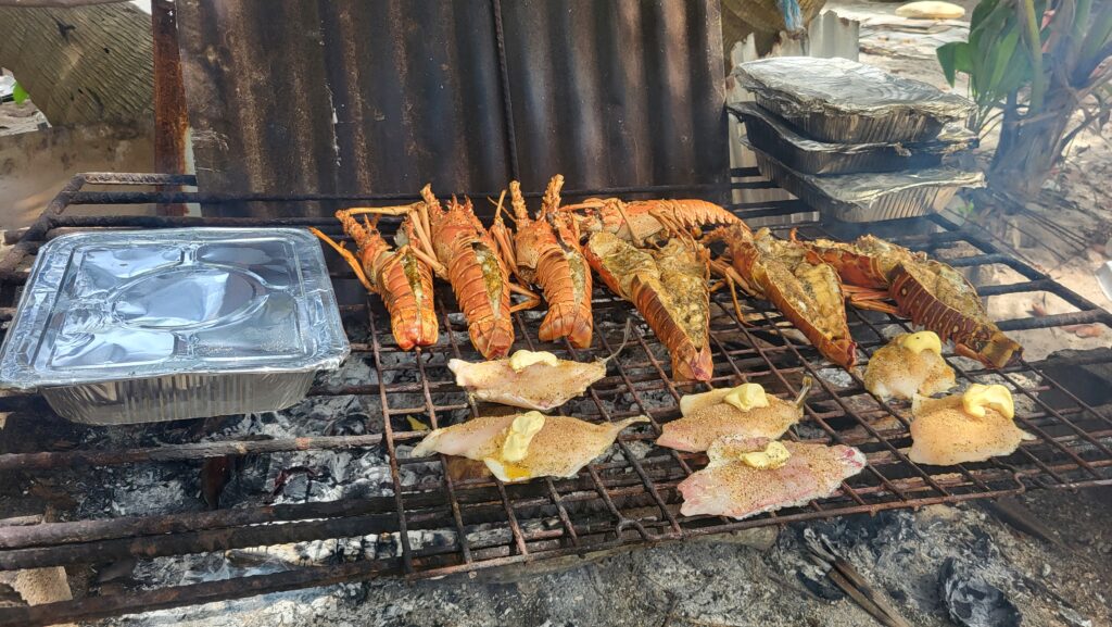 "Rows of Caribbean lobster tails sizzling over hot coals during an authentic Belizean beach BBQ."