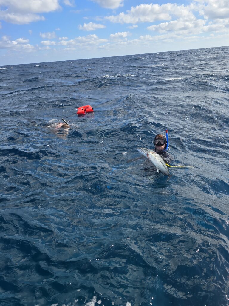 "A snorkeler in the deep blue Caribbean Sea holding up a freshly speared spanish mackrel during a private Belize excursion."