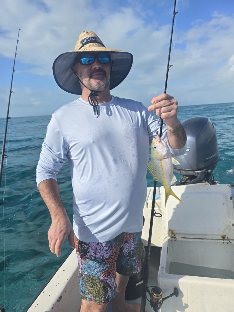 "A happy guest in a sun hat holding up a yellowtail snapper caught on a Fish 101 boat charter."
