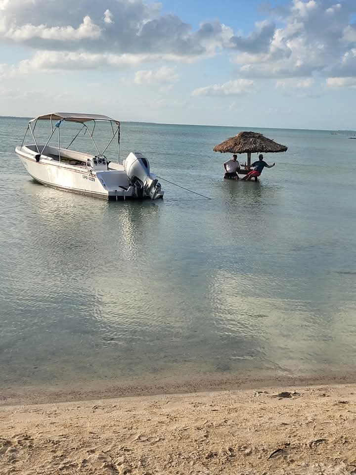 "A peaceful view of the Fish 101 boat anchored near a tropical thatched-roof hut in shallow water."