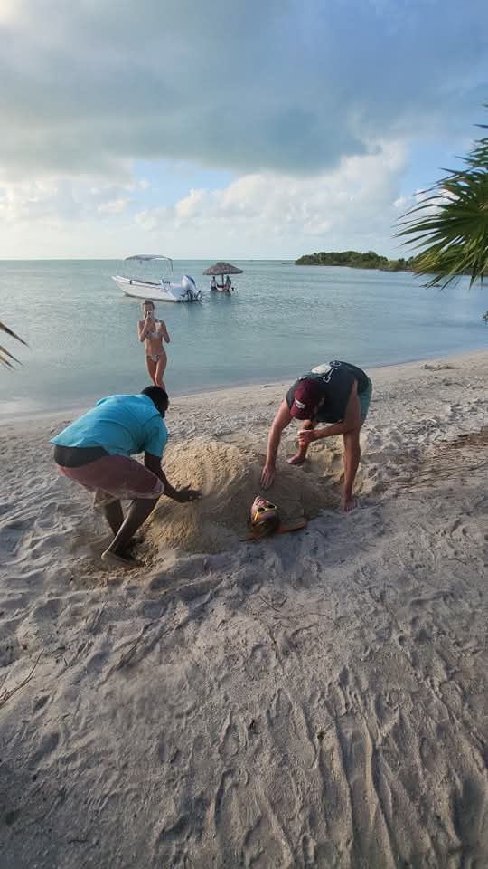"A local guide preparing a beach area for a private island lunch and BBQ after a morning of reef fishing in Belize."
