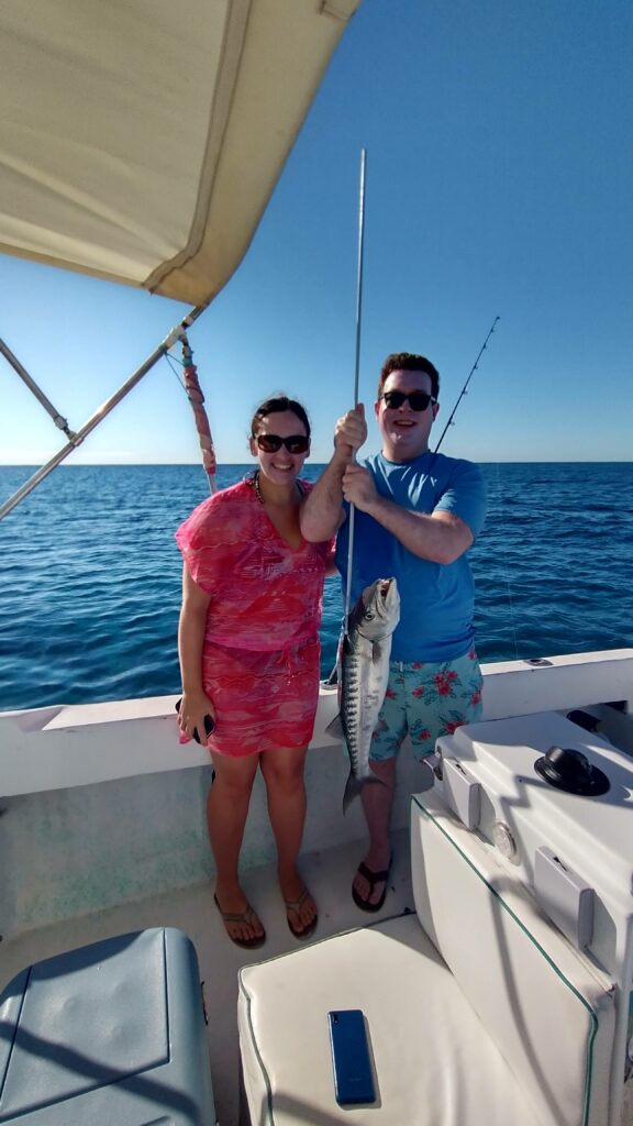 "A smiling couple posing on the boat deck while holding up a fresh barracuda they caught together."